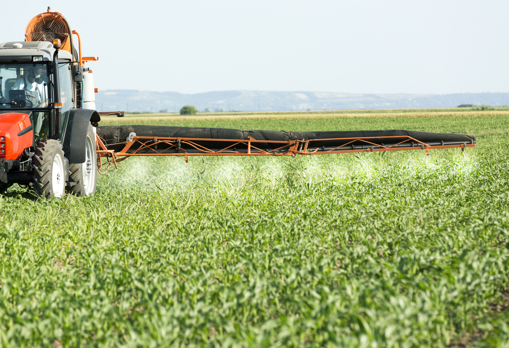 Farmer in red tractor spraying soybean field